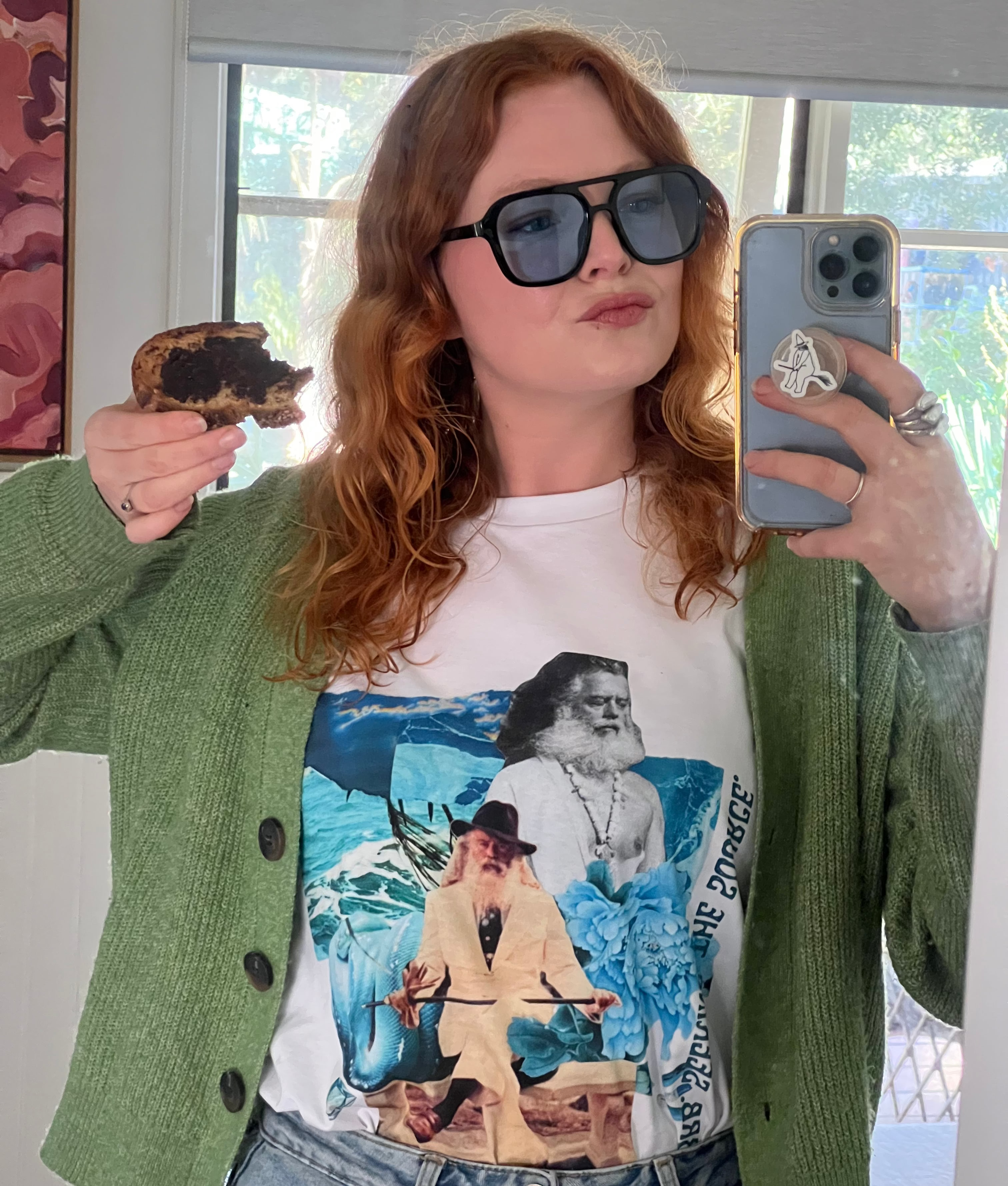 Person wearing a graphic t-shirt with a design, holding a phone and a vegemite on toast.